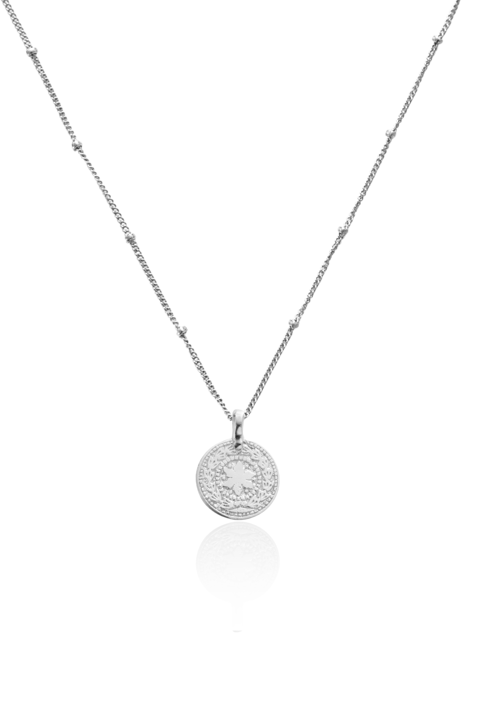 Close-up of silver coin pendant featuring sun and moon symbols